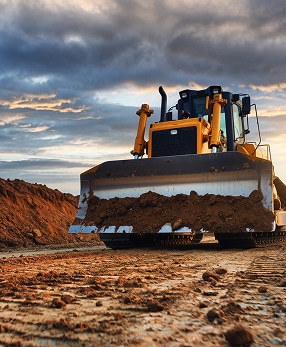 Bulldozer en action: L'engin de terrassement essentiel au BTP. Engin de chantier puissant: un bulldozer jaune effectuant des travaux de terrassement sous un ciel dramatique au soleil couchant.